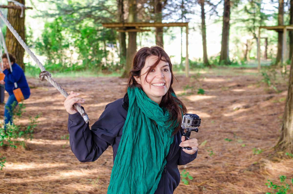 Andrea Orellana sonríe en un bosque, con una bufanda verde.